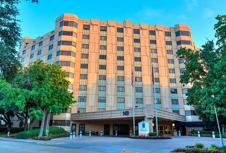 A large hotel building with trees on the side, set against a clear blue sky.