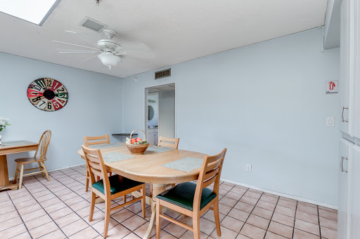 A cozy dining area featuring a wooden table surrounded by chairs, complemented by a ceiling fan and light blue walls.