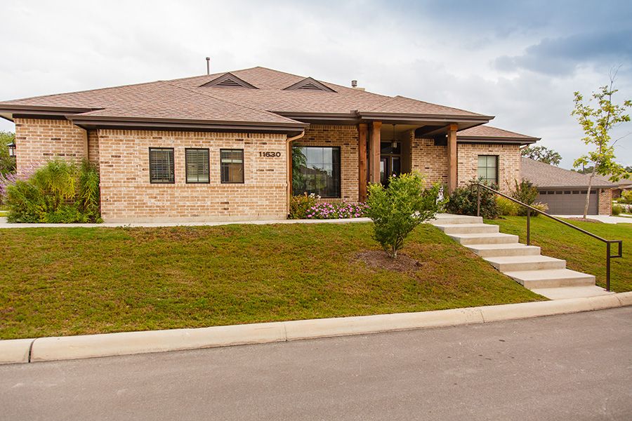 A single-story brick house with a well-maintained lawn in a suburban area.