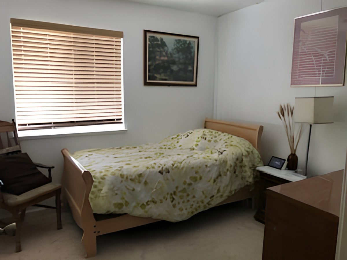 A cozy bedroom with a single bed featuring a floral bedspread, a window with blinds, and a painting on the wall.