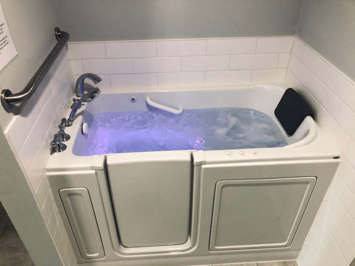 A walk-in bathtub filled with water, featuring a safety handle and tile backsplash.