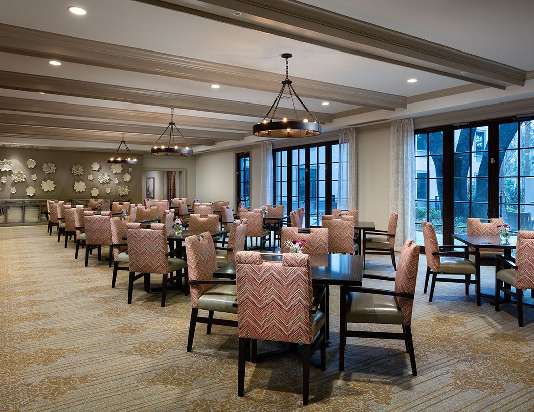 A spacious dining room with neatly arranged tables and chairs, illuminated by elegant lighting fixtures.