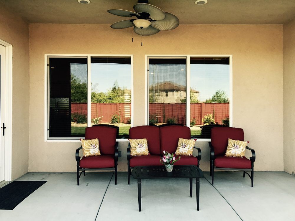 A cozy patio setup with red cushioned chairs and decorative pillows in front of large windows.