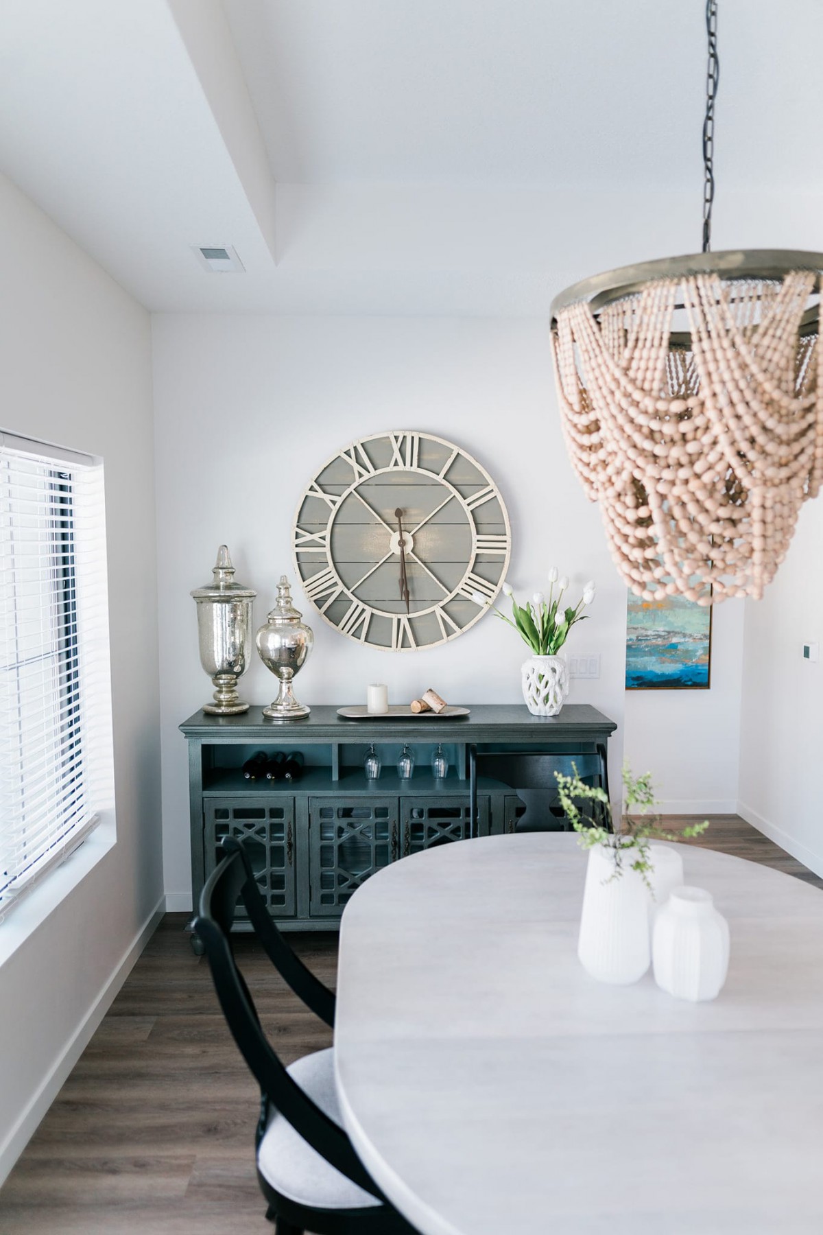A stylishly decorated dining area featuring a large wall clock, an elegant chandelier, and a sideboard with decorative items.
