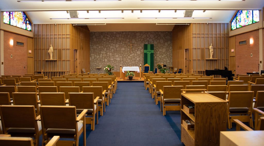 A peaceful chapel interior with rows of seating, an altar, and a prominent cross at the front.