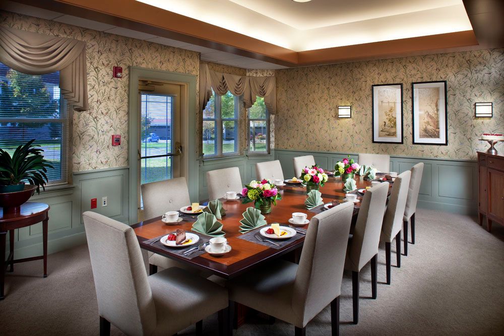 An elegantly decorated dining room with a long table set for a formal meal, featuring cushioned chairs and floral centerpieces.
