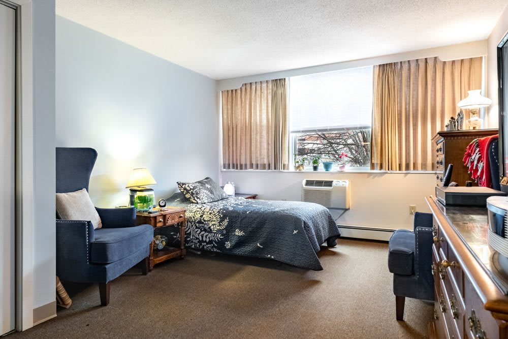 A cozy bedroom featuring a bed, chairs, and a window with curtains.