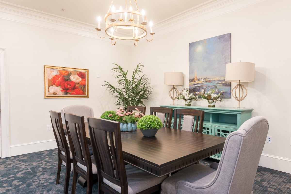A beautifully decorated dining room with a centerpiece chandelier, art on the walls, and indoor plants adorning the space.