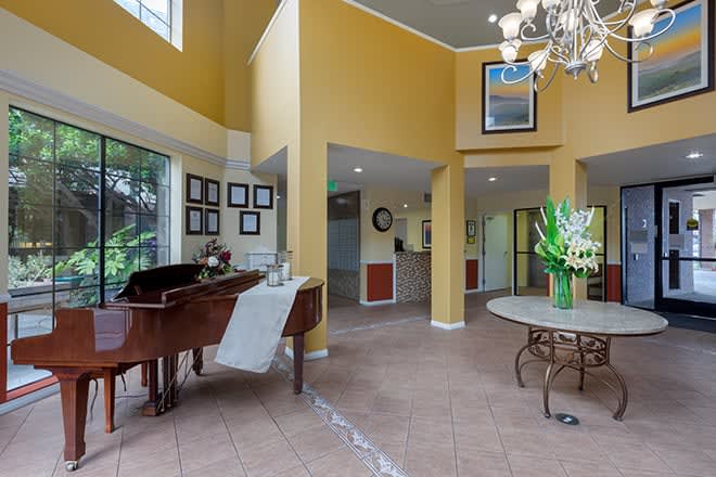 A spacious living room with a grand piano, elegant chandelier, and large windows allowing natural light.