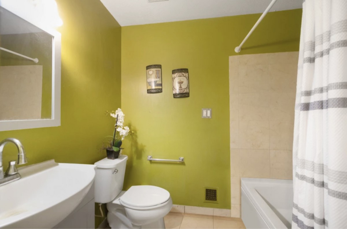 A modern bathroom with green walls and minimalist decor, featuring a toilet, sink, and bathtub.