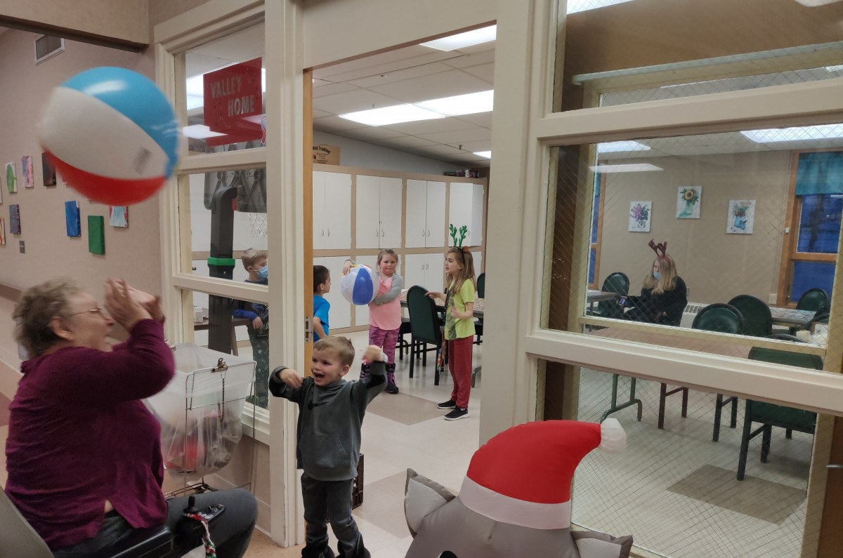 Children playing with balloons indoors near a large window.