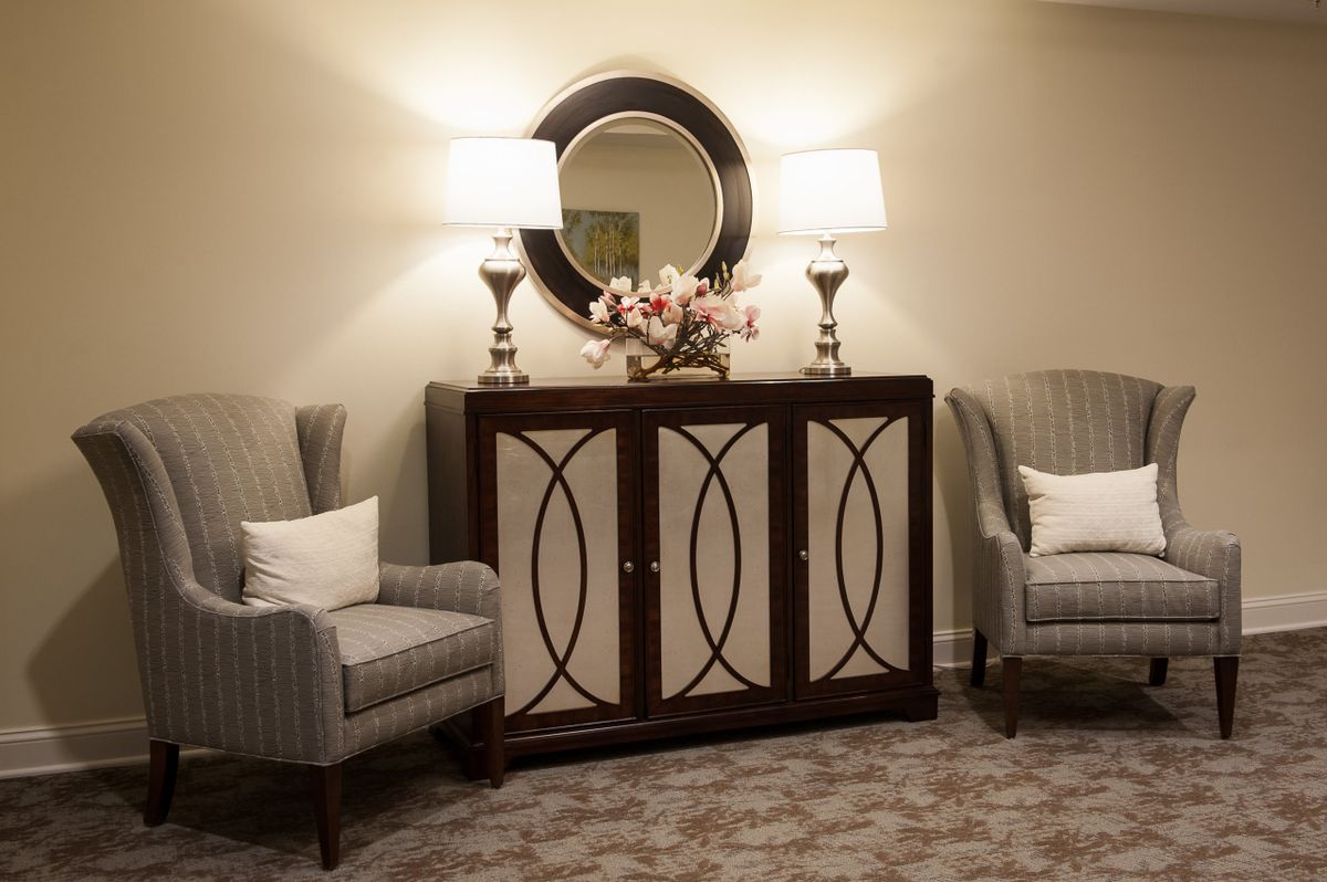 A cozy living room corner featuring two armchairs, a decorative cabinet with a mirror, and two elegant lamps.