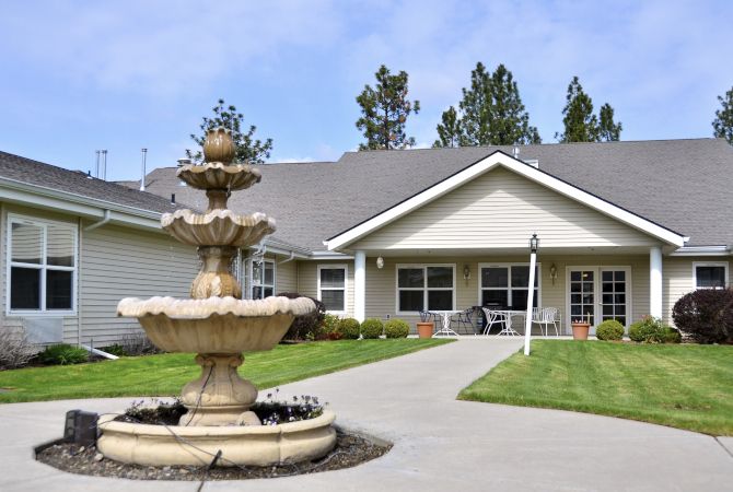A building with a three-tiered fountain in the foreground, surrounded by well-maintained landscaping and a pathway leading to the entrance.