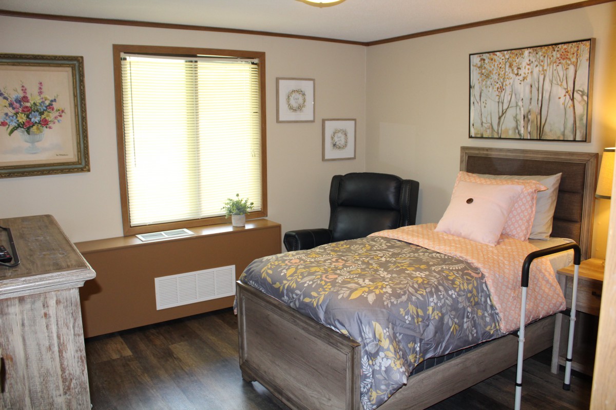 A cozy bedroom with a single bed, an armchair, and a window providing natural light.