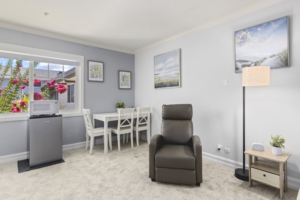 A cozy living room featuring a leather recliner chair, a dining table with chairs, wall art, and a lamp on a carpeted floor.