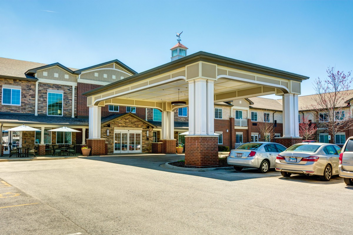 A view of a building with a covered entrance and parked cars in the driveway.