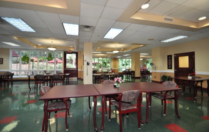 A spacious dining area with tables and chairs, featuring large windows and indoor plants.