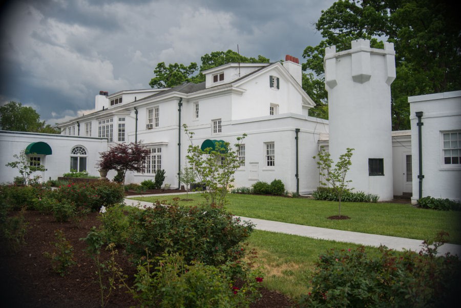 A large white house with a well-maintained garden and a cloudy sky in the background.