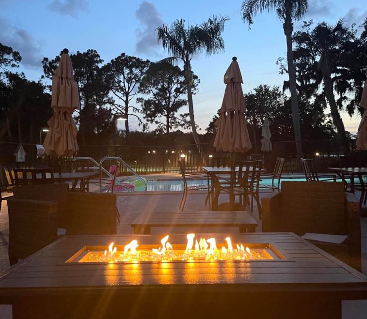 A cozy evening view by the fire pit near a pool, surrounded by palm trees.