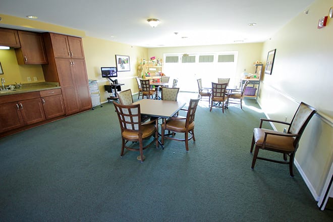 A bright dining area with multiple tables and chairs arranged on a carpeted floor.
