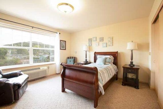 A cozy bedroom with a single bed, nightstands, and ample natural light from a large window.