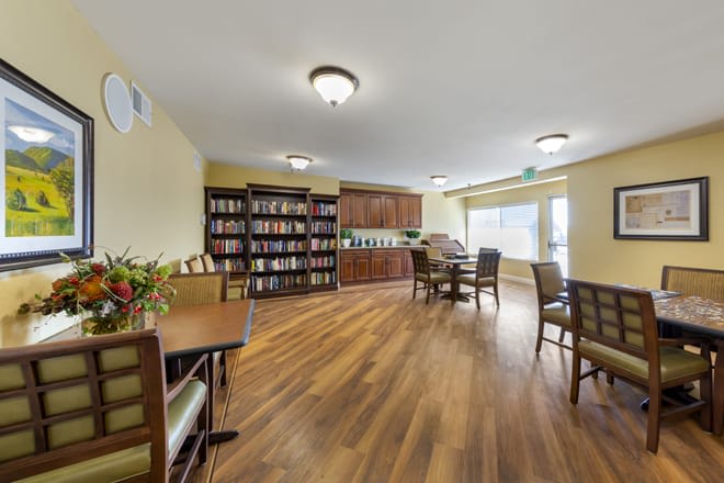 A cozy library with bookshelves, tables, and chairs, featuring a warm wooden floor and soft lighting.