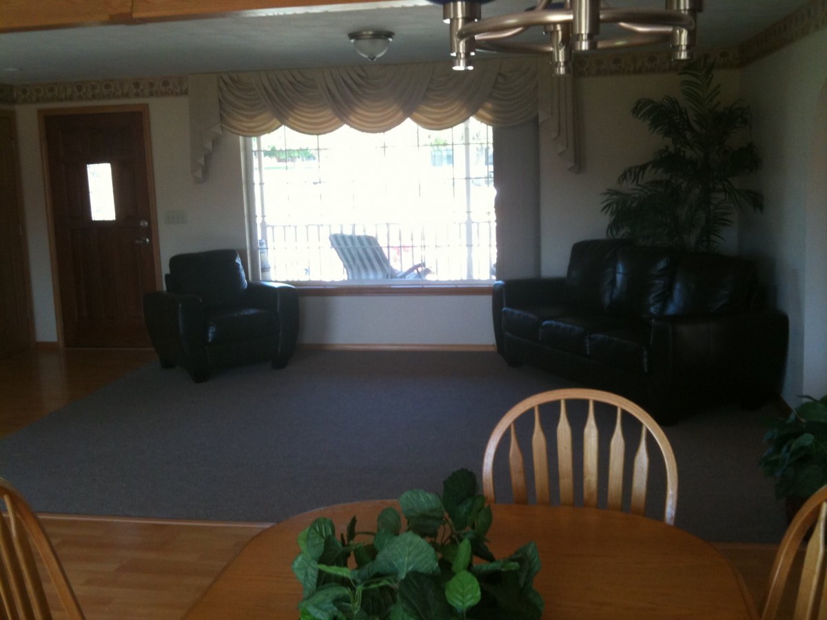 A cozy living room with two chairs, a large window, and a dining table with an indoor plant.