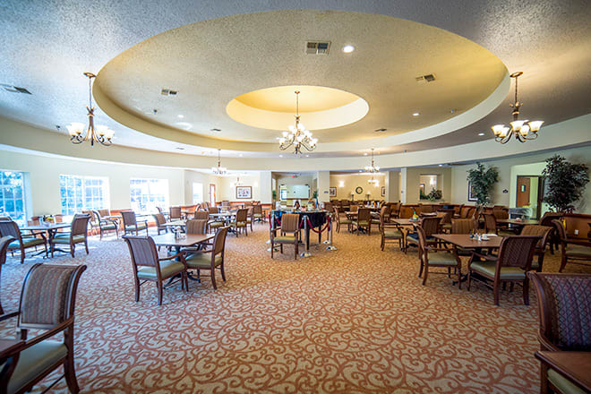 A spacious dining area with tables and chairs, featuring elegant ceiling lighting.