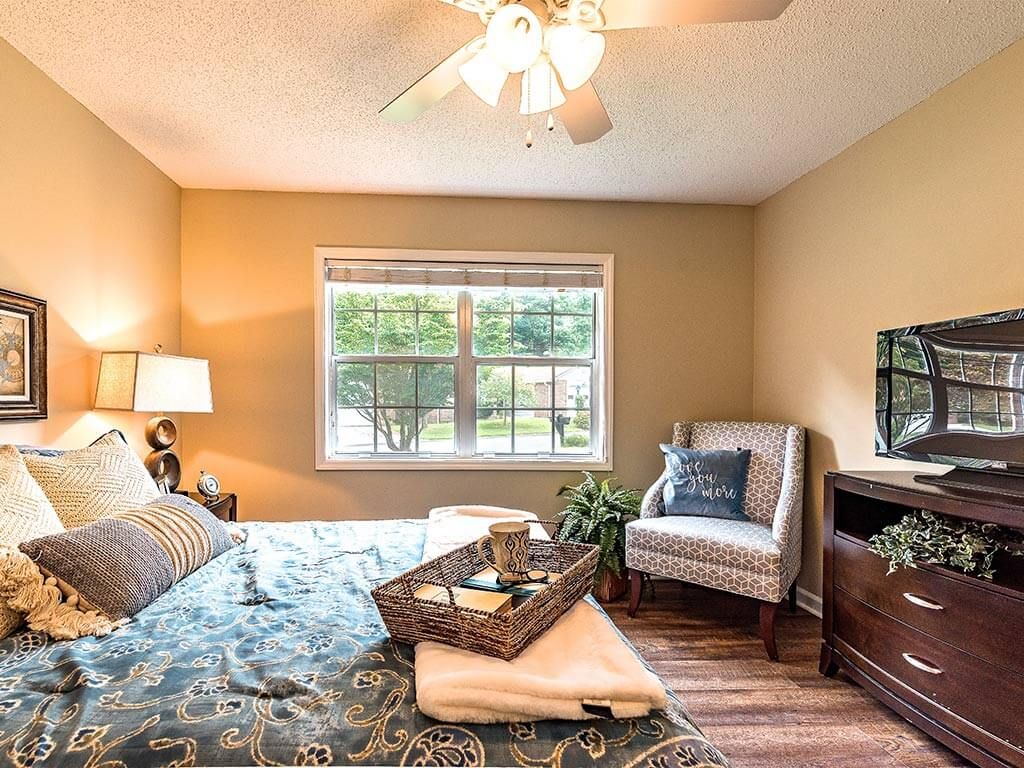A cozy bedroom with a ceiling fan, large window, and comfortable furnishings.