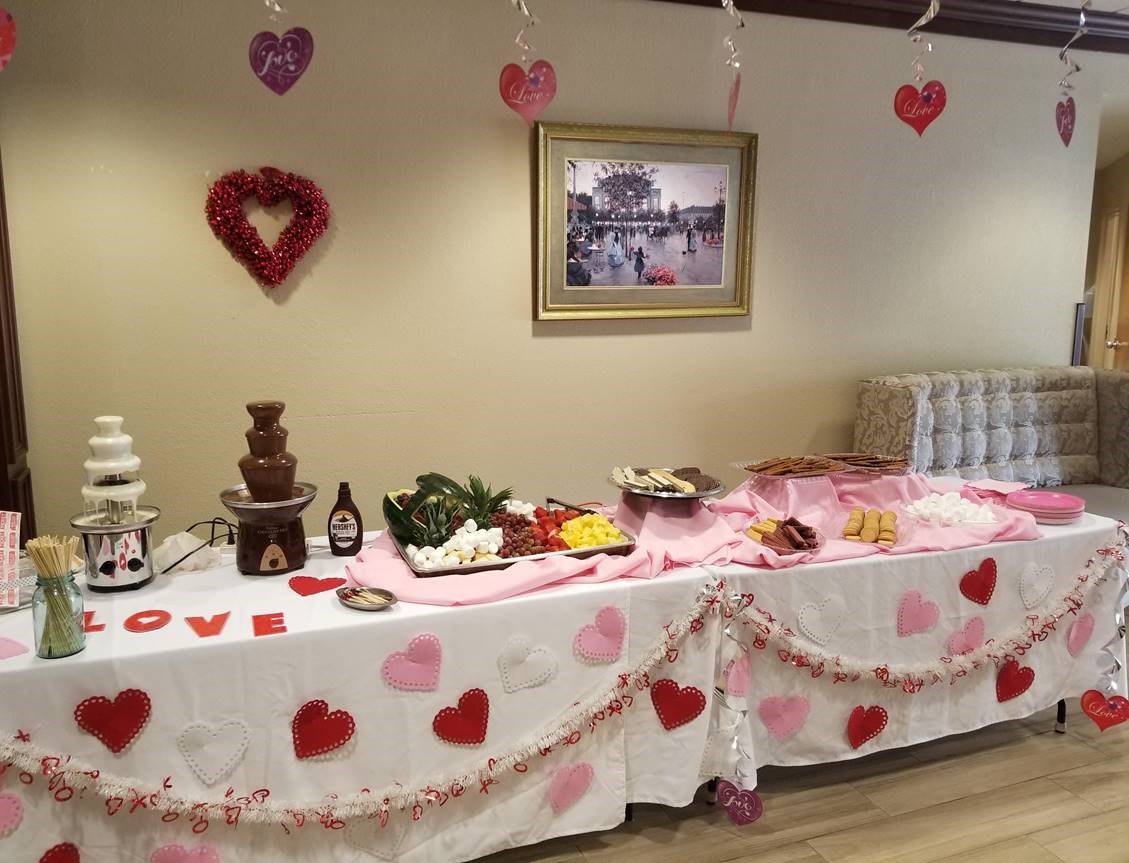 A Valentine's Day themed party table decorated with hearts and featuring a chocolate fountain along with various snacks.