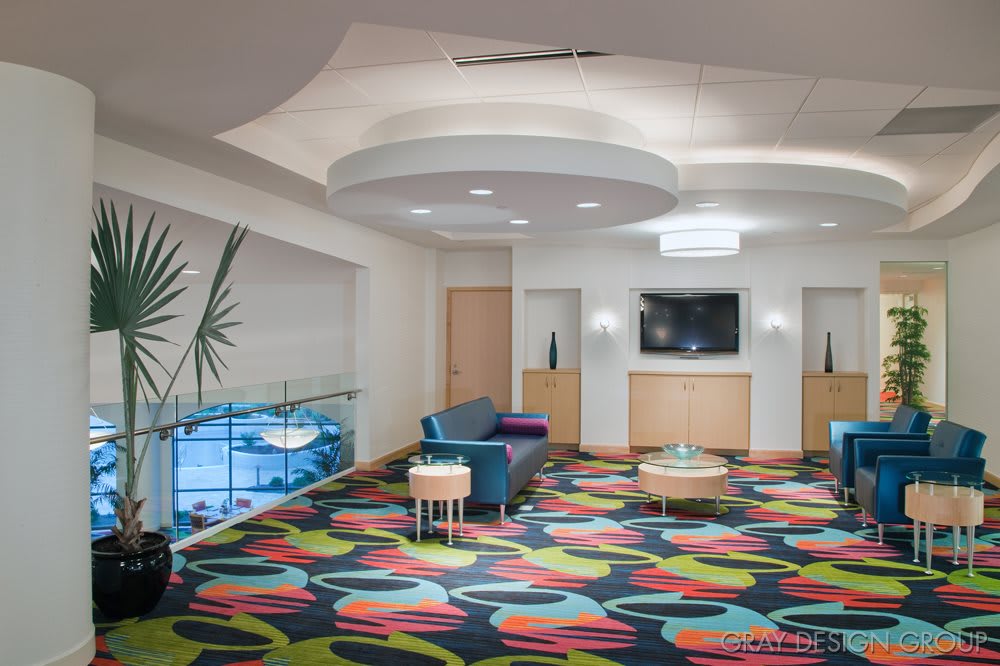 A modern lobby featuring colorful carpets, minimalist furniture, and a wall-mounted television.