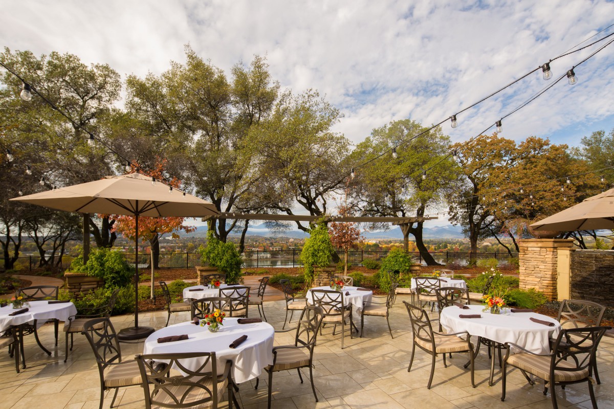 A serene patio setup with tables and chairs, surrounded by trees and overlooking a scenic view.