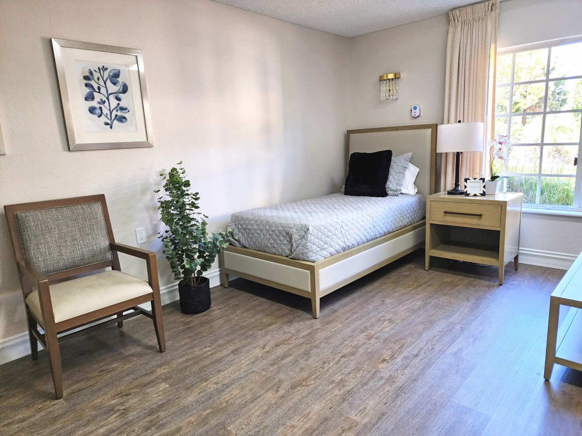 A minimalistic bedroom with a single bed, chair, and potted plant.