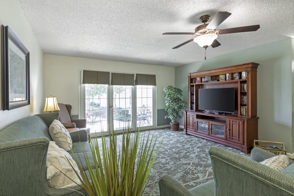 A cozy living room with a television, comfortable seating, and large windows.