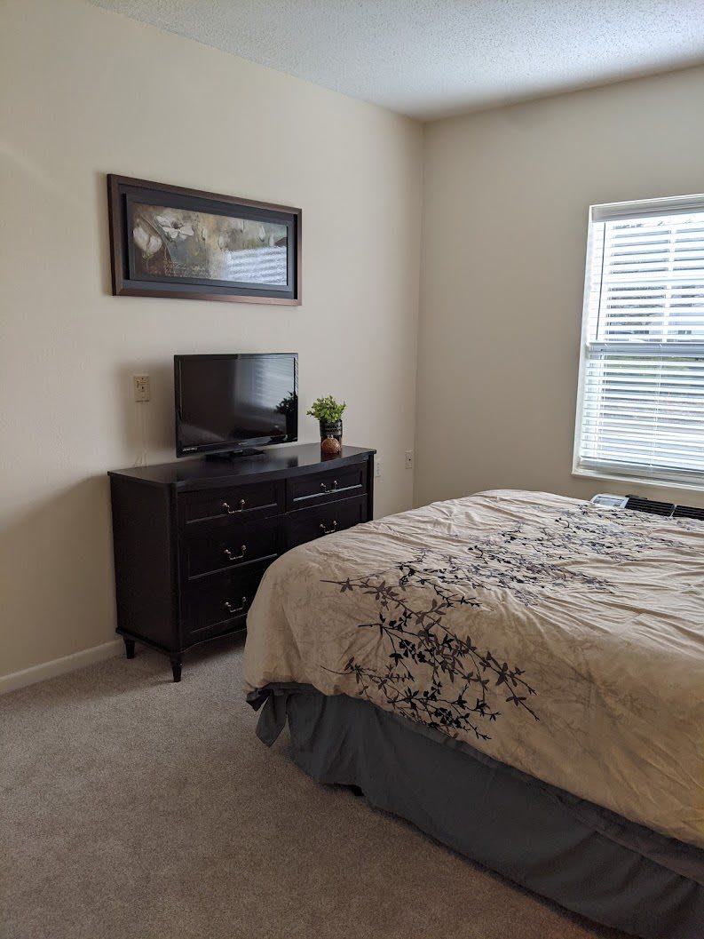 A cozy bedroom with a bed, dresser, and television near a window.