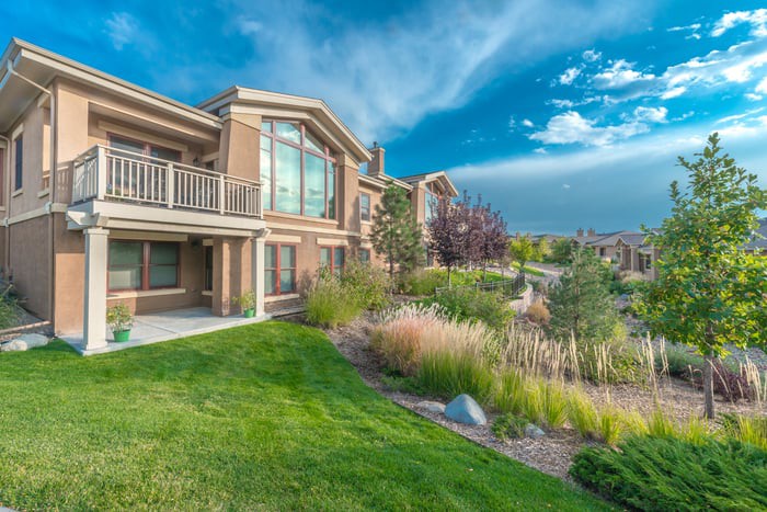 A modern house with a well-maintained front yard and picturesque landscaping under a partly cloudy sky.