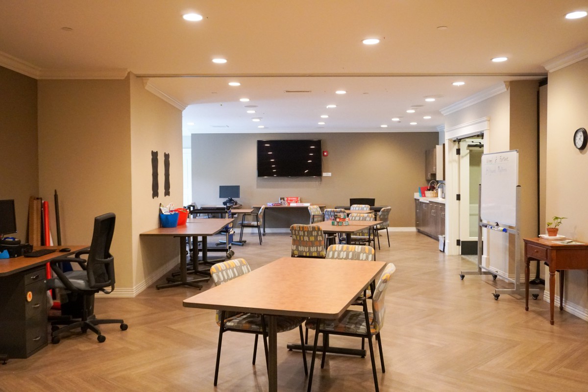 A modern office workspace featuring tables, chairs, and a large screen.