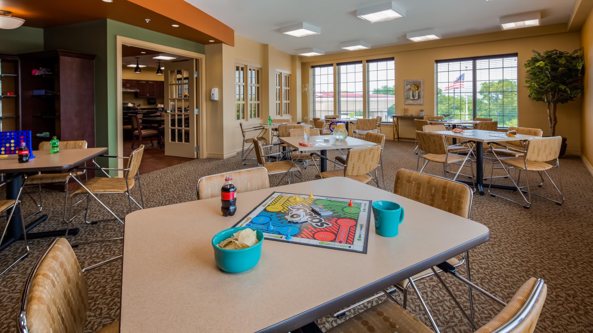 A cozy dining area with tables and chairs, featuring a board game setup and drinks on the table.