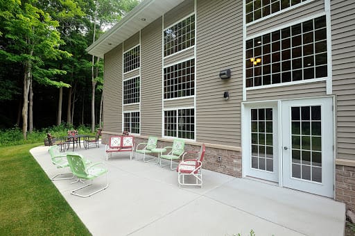 A modern patio with colorful chairs against a building's glass windows, surrounded by trees.