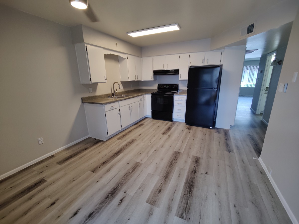 A modern kitchen with white cabinets and wood flooring.