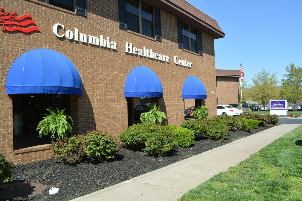 A brick healthcare center with blue awnings and landscaped surroundings.