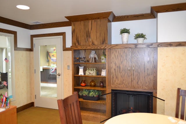 A cozy living room featuring wooden built-in shelves and a fireplace, decorated with various ornaments and potted plants.