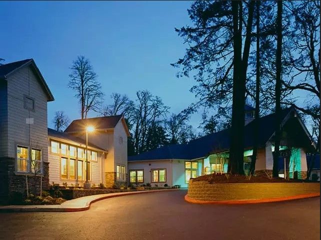 A well-lit building surrounded by tall trees during the evening.