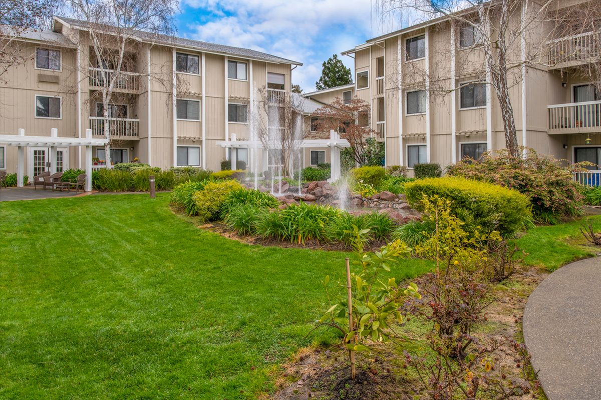 A residential apartment complex featuring a well-maintained lawn and a central fountain.