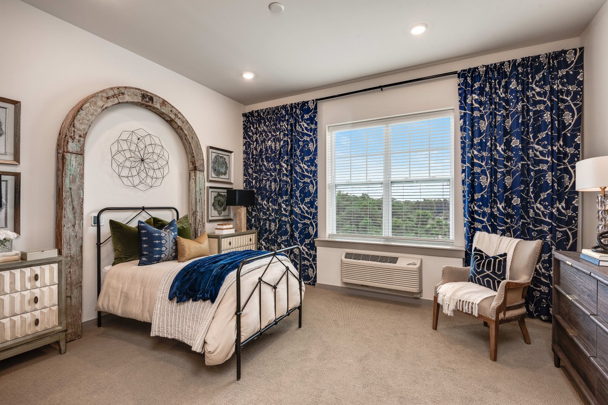 A cozy bedroom with a stylish interior, featuring blue patterned curtains and a metal-framed bed.