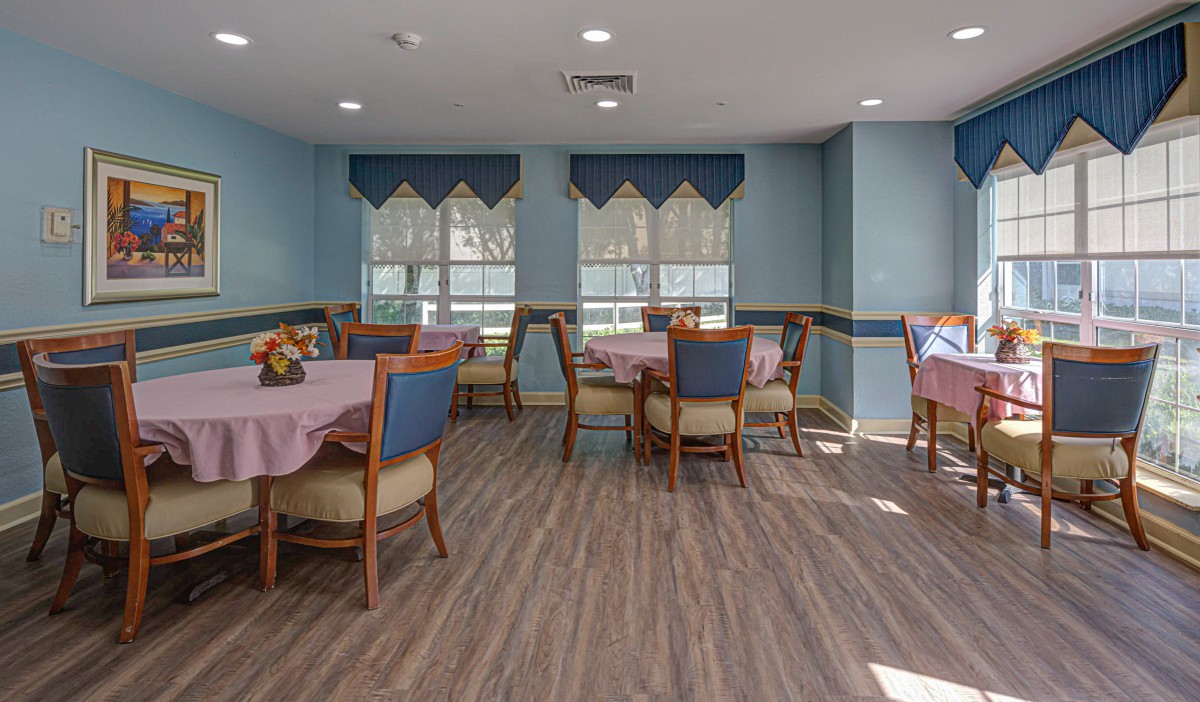 A well-lit dining area with neatly arranged tables and chairs, featuring large windows with blue curtains.