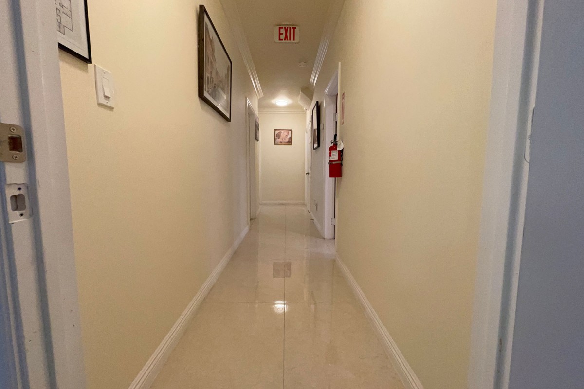 A well-lit hallway with paintings on the walls, an exit sign, and a fire extinguisher.