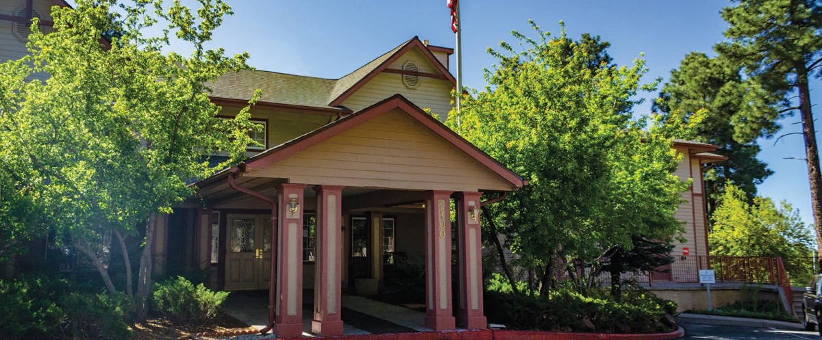 A house with a covered porch and columns, surrounded by trees, featuring a flagpole.