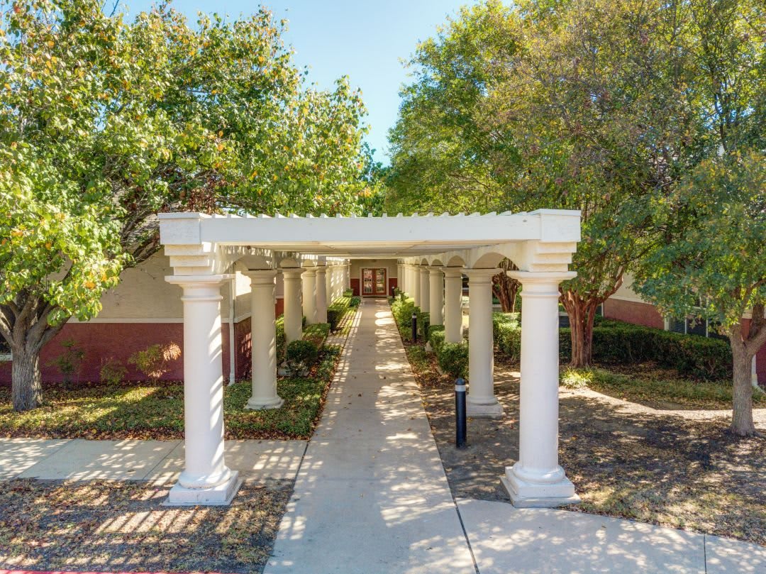 A beautifully designed outdoor pathway with columns and a pergola, surrounded by lush trees.