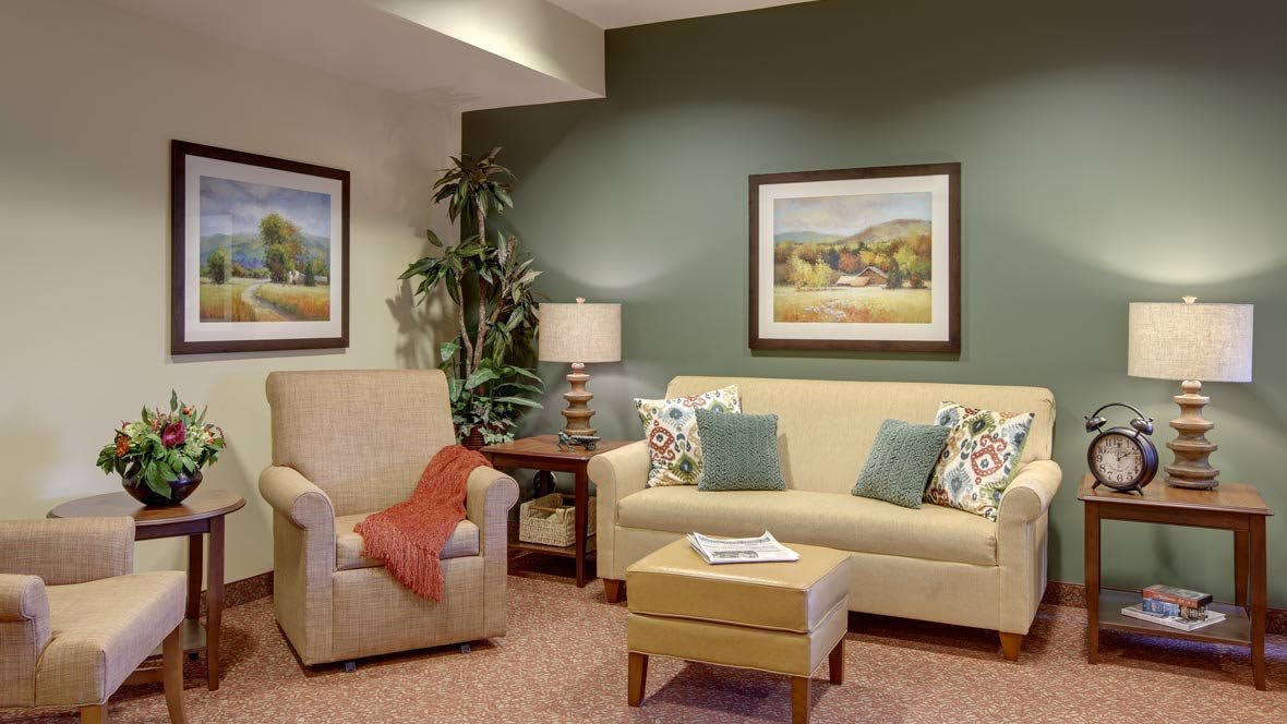 A cozy living room with a beige sofa, armchair, and decorative elements including a potted plant and framed wall art.